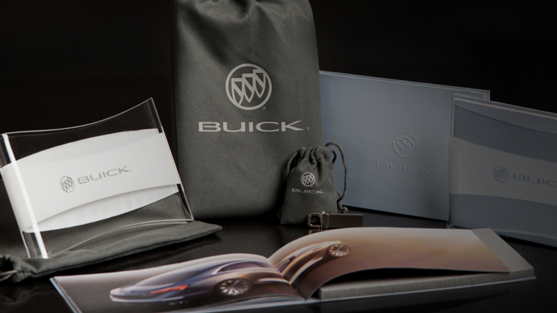 The complete Buick Avenir press kit photographed in low light: pouches, lucite sleeve, embossed books, and open booklet